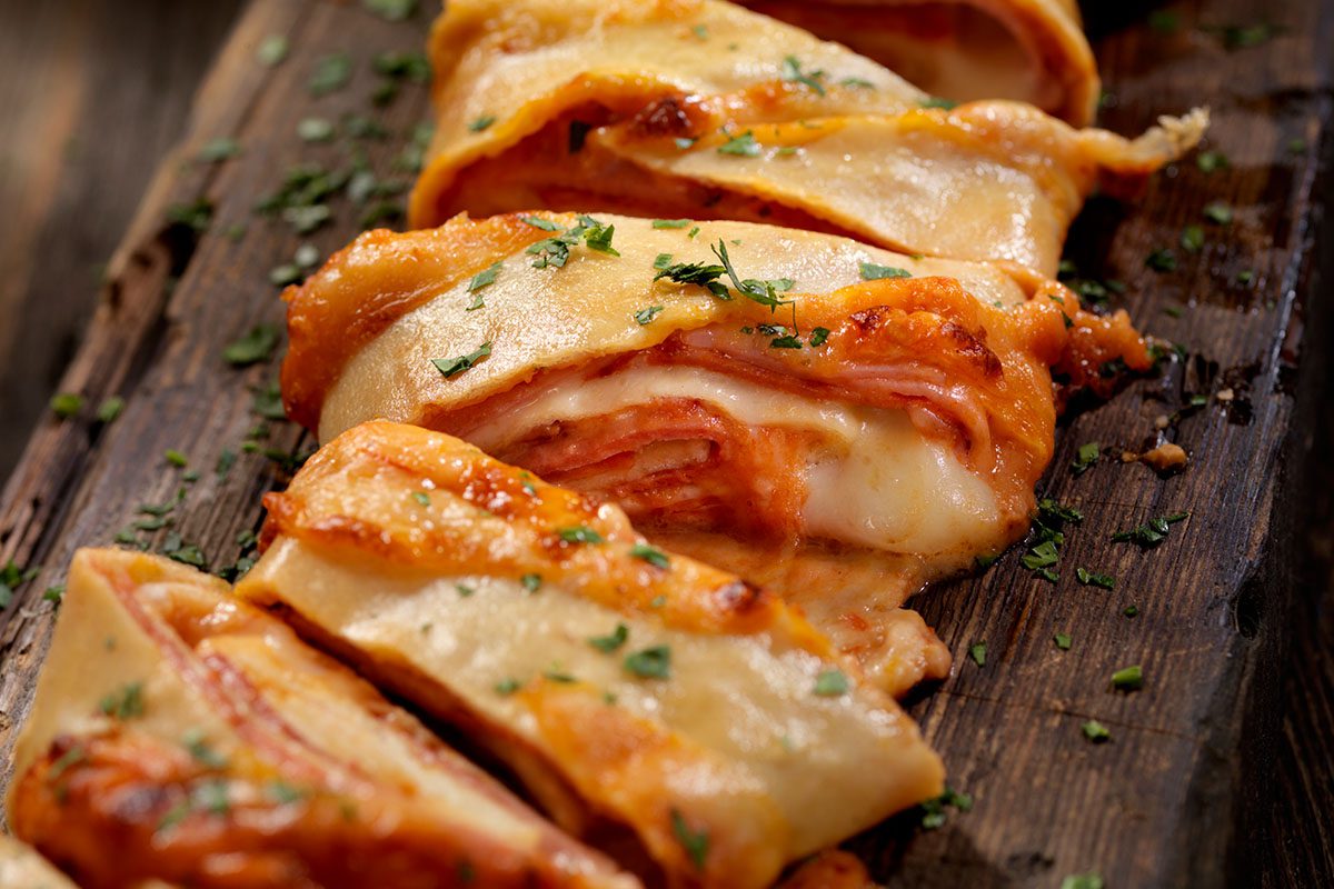 A wooden cutting board topped with lasagna.