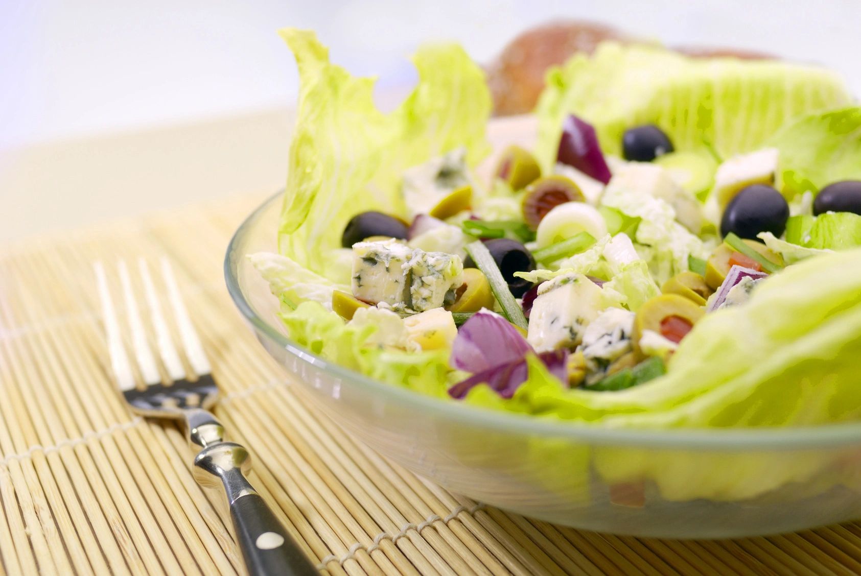 A bowl of salad with lettuce, olives and cheese.